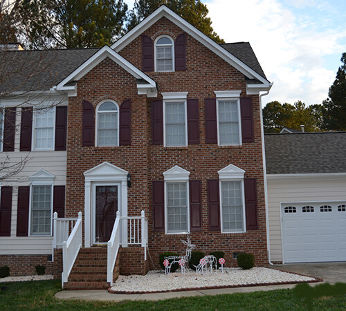 A brick house with a newly shingled roof by Housetop Roofing & Home Improvement in Wake Forest, NC