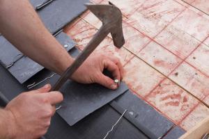 Roofing contractor hand-nailing shingles to a roof.