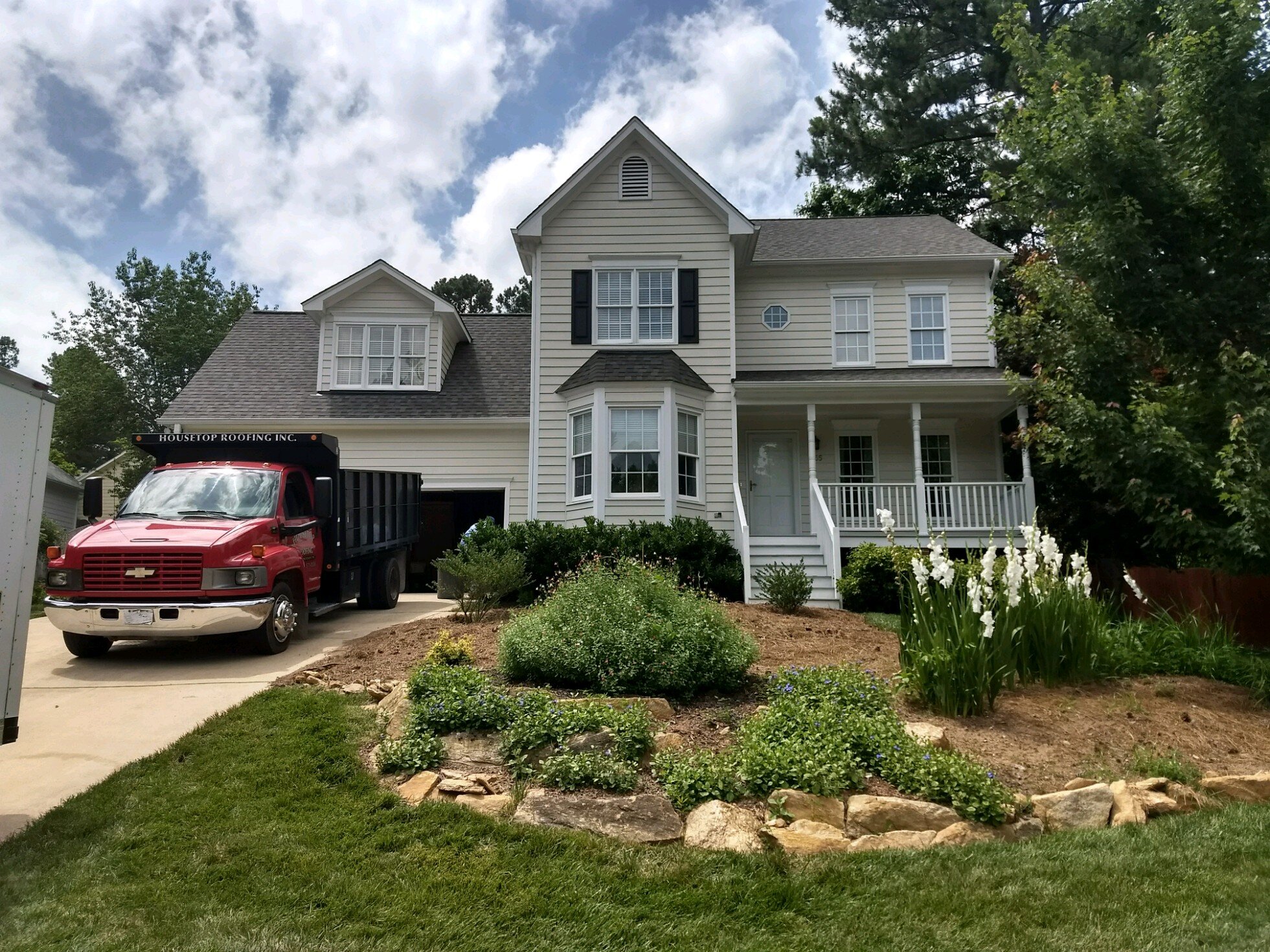 A house with a new roof with dormers and multiple porches reroofed by Housetop Roofing.