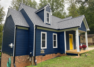 A blue house with a newly shingled roof and black gutter installation from Housetop Roofing in Raleigh, NC
