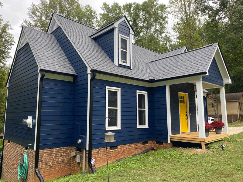 A blue house with a newly shingled roof and black gutter installation from Housetop Roofing in Wake Forest, NC