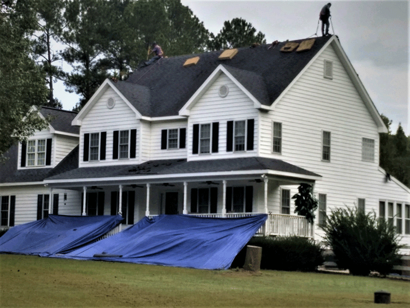 A home with a new roof being installed in Wake Forest and a blue tarp protecting shrubbery and landscaping.