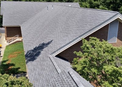 Aerial view of a new gray architectural shingle roof with ridge vents on a brick building in Raleigh, NC.