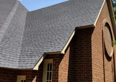 Close-up of a new gray shingle roof on a brick building gable with a round window in Raleigh, NC.