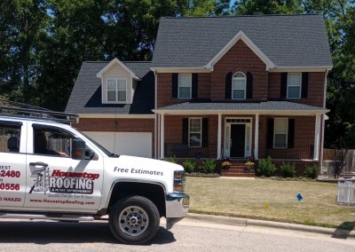 Brick two-story colonial with a new dark gray shingle roof and a Housetop Roofing truck at the curb.