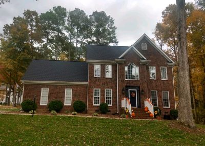 Brick colonial-style home with a new dark architectural shingle roof in autumn.