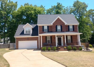 Brick two-story home with a front porch, bonus room dormer, and new gray architectural shingle roof.