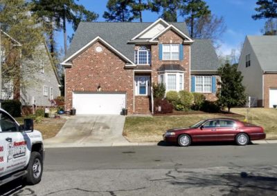 Two-story brick home with a new gray shingle roof and a Housetop Roofing truck parked out front.