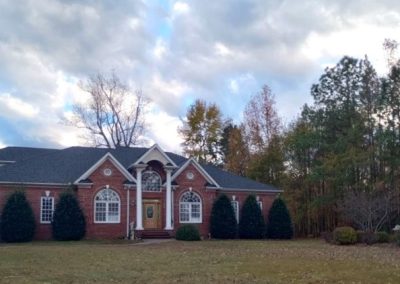 Wide brick ranch home with a columned front entry and a new dark shingle roof under a cloudy sky.