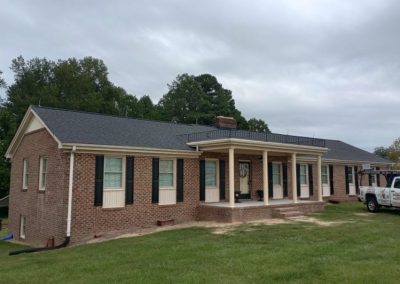 Long brick ranch home with a columned front porch and a newly installed dark gray shingle roof.