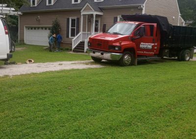 Housetop Roofing red dump truck at a Cape Cod home with three dormers during a roof replacement.