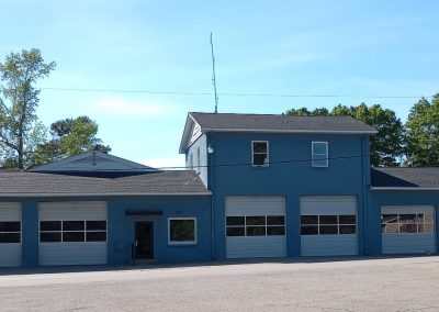 New architectural shingle roof on a blue two-story commercial garage building with multiple bay doors.