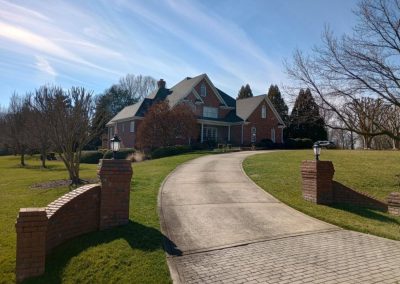 Large brick estate home on a hill with a brick-pillared driveway and a new shingle roof.