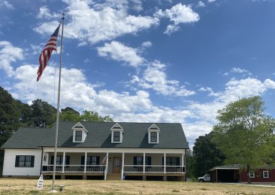 White farmhouse with three dormers, a long front porch, and a new green architectural shingle roof.
