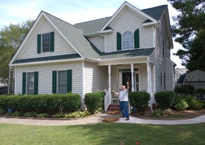 Homeowner cheering in front of a two-story home with a new gray-green architectural shingle roof.