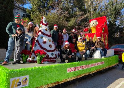 Housetop Roofing team in Santa hats on a green holiday float in the ABC11 Raleigh Christmas Parade.