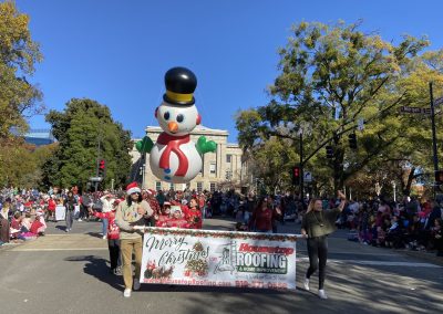Housetop Roofing team carrying a Merry Christmas banner ahead of a giant snowman balloon in downtown Raleigh.