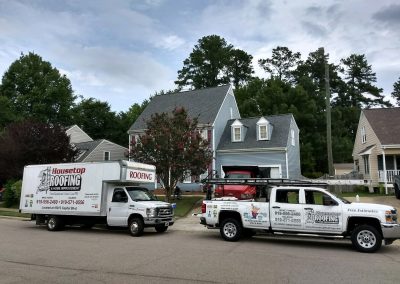 Housetop Roofing box truck and pickup parked at a blue two-story home during a roof replacement.