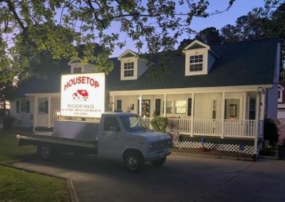 Housetop Roofing & Home Improvements sign truck parked in front of a dormered Cape Cod home at dusk.