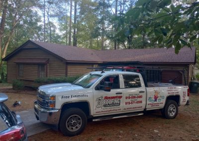 Housetop Roofing pickup truck parked at a wood-sided ranch home with a new brown shingle roof.