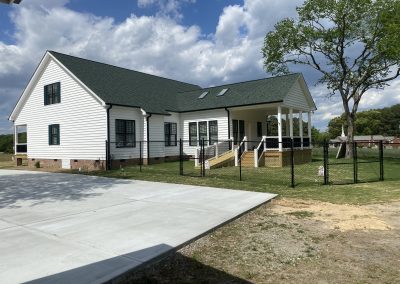 Newly built white farmhouse with a green architectural shingle roof and covered side porch.