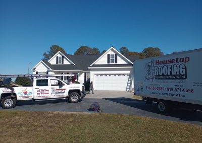 Housetop Roofing trucks parked at a newly built white home with a fresh shingle roof.