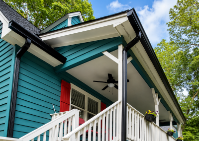 Close-up of a teal home's front porch with new black gutters, downspouts, and a dark shingle roof.