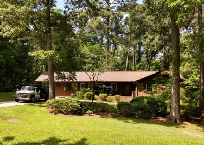 Ranch home on a wooded lot with a new brown shingle roof and a work truck in the driveway.