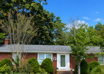 Red brick ranch home with a new gray shingle roof surrounded by mature trees.
