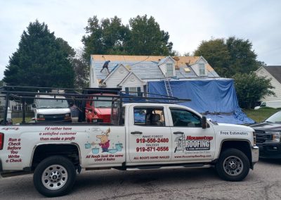 Housetop Roofing crew tearing off an old roof with tarps protecting the yard and the company truck out front.
