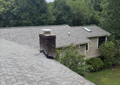 Close-up of a new light gray shingle roof around a brick chimney and skylight.