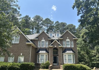 Large brick home with a new gray shingle roof and standing seam metal roofing over the bay windows.