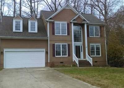 Tan two-story home with twin dormers over the garage and a new dark shingle roof.