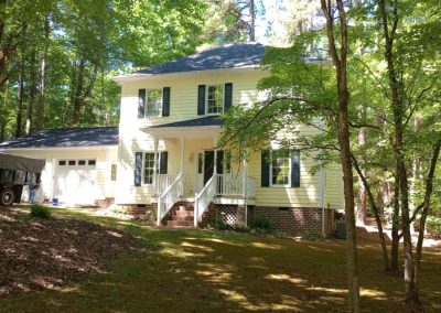 Yellow two-story home among trees with a new gray architectural shingle roof.