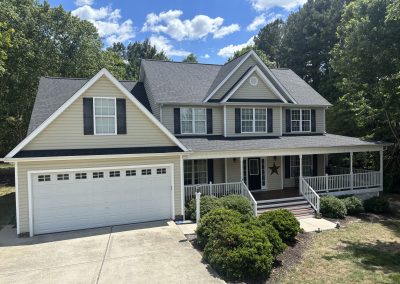 Two-story tan home with a wraparound porch and a new gray architectural shingle roof.